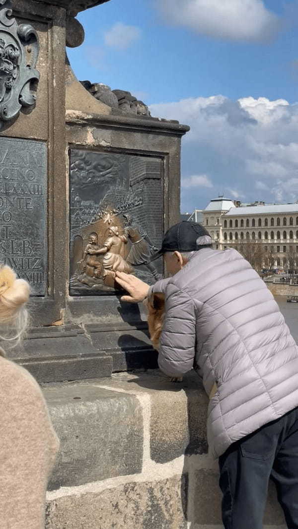 プラハの観光地で目撃された微笑ましい光景。撫でると願いが叶うとされるプレートを、おじいさんが愛犬にもナデナデさせていました！